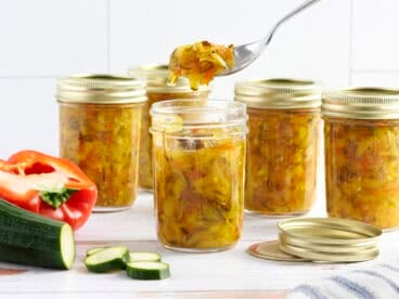 Side view of jars of zucchini relish, is a spoon taking some from one jar.