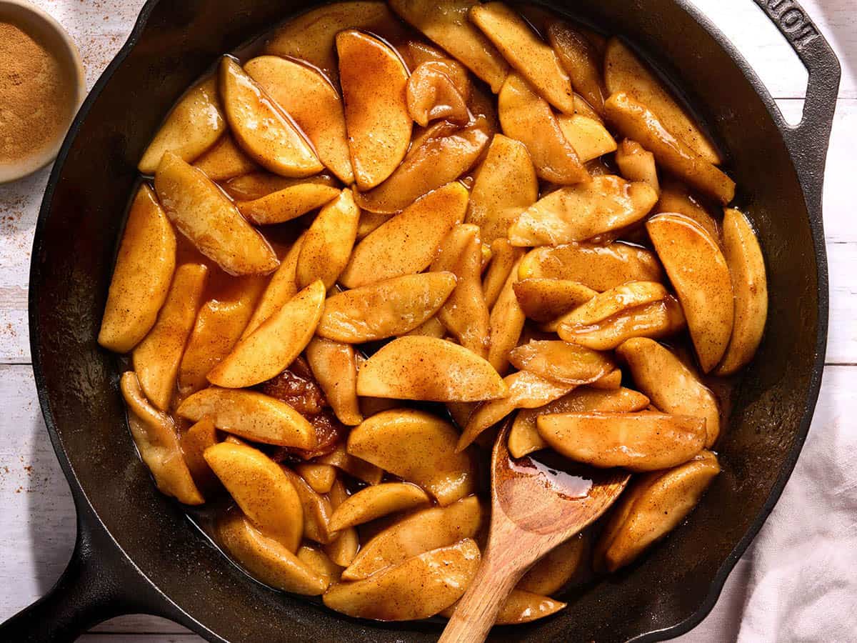 Overhead view of a skillet of fried apples with a wooden spoon stirring them.