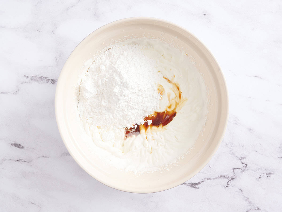 Powdered sugar, vanilla extract and heavy cream in a mixing bowl.