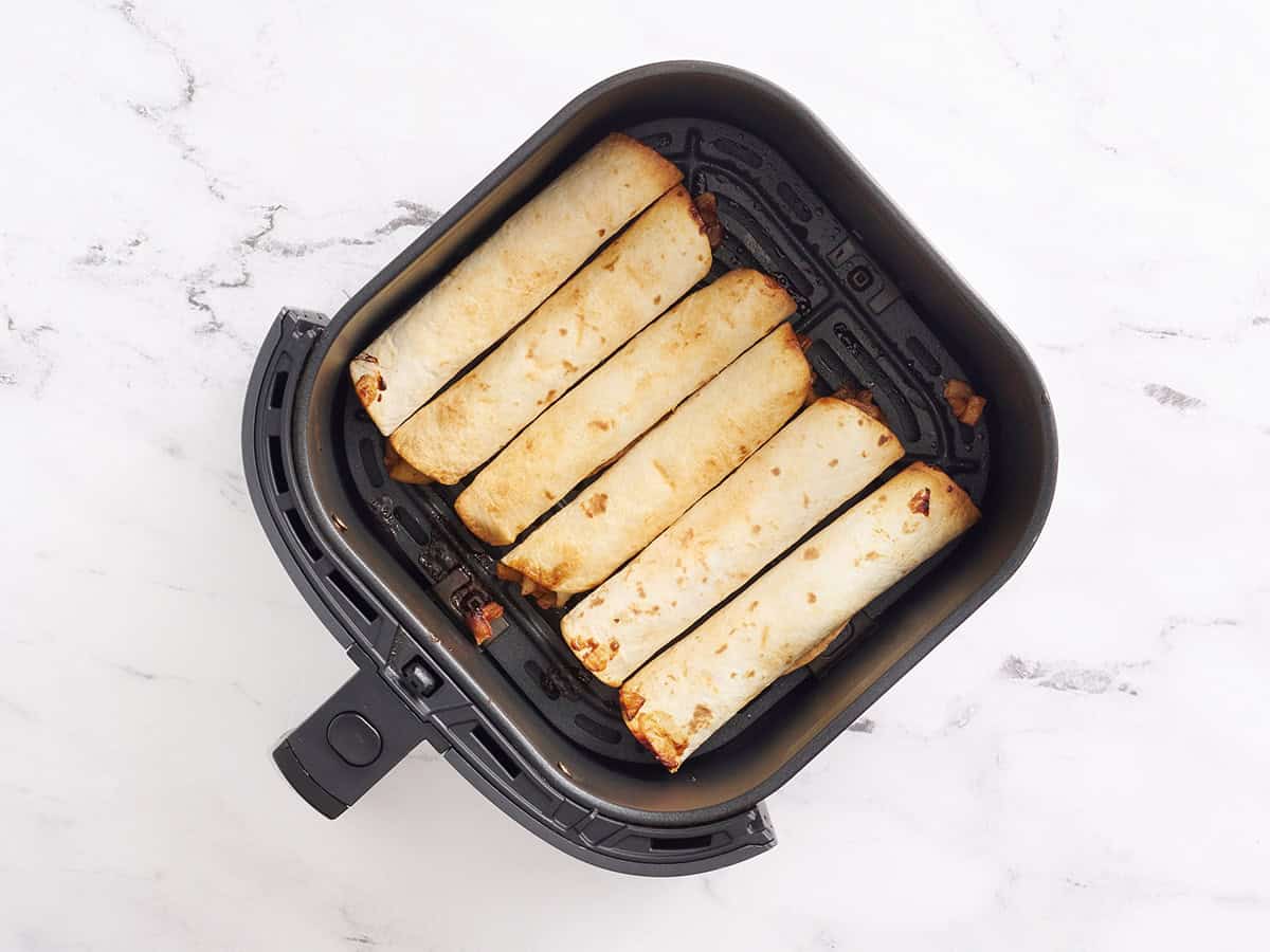 Air fried apple flautas in an air fryer basket.