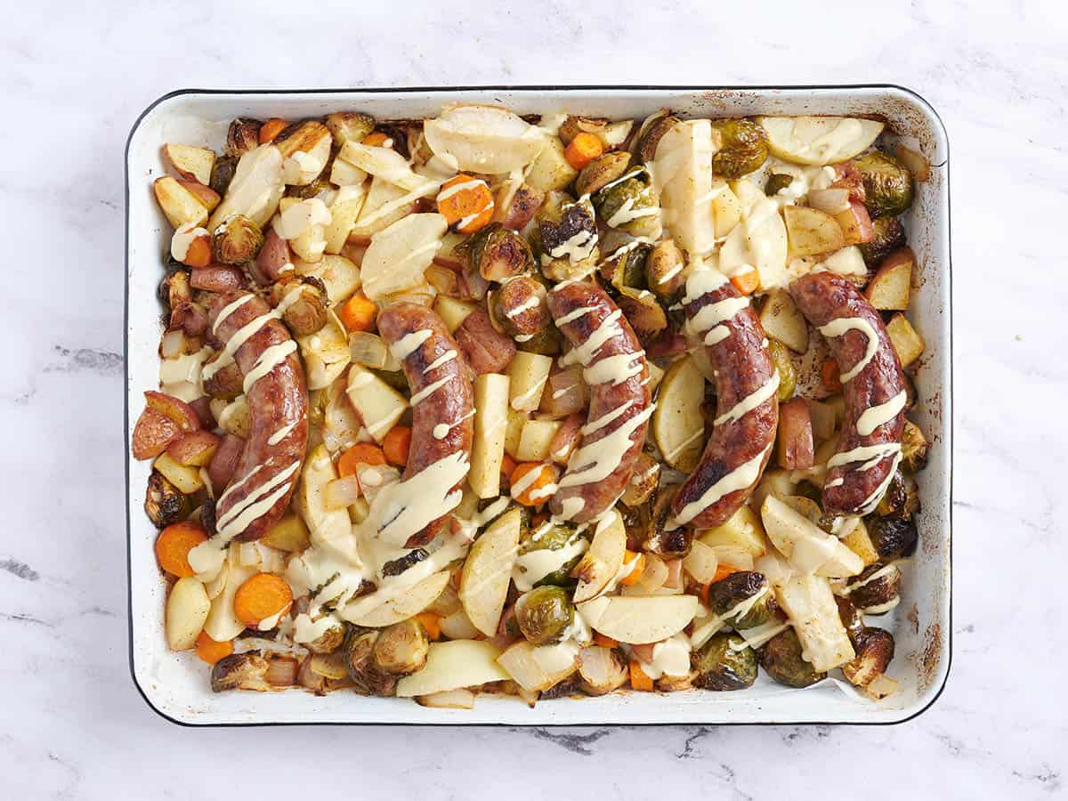 Oktoberfest sheet pan brats drizzled with mustard sauce on a baking sheet.