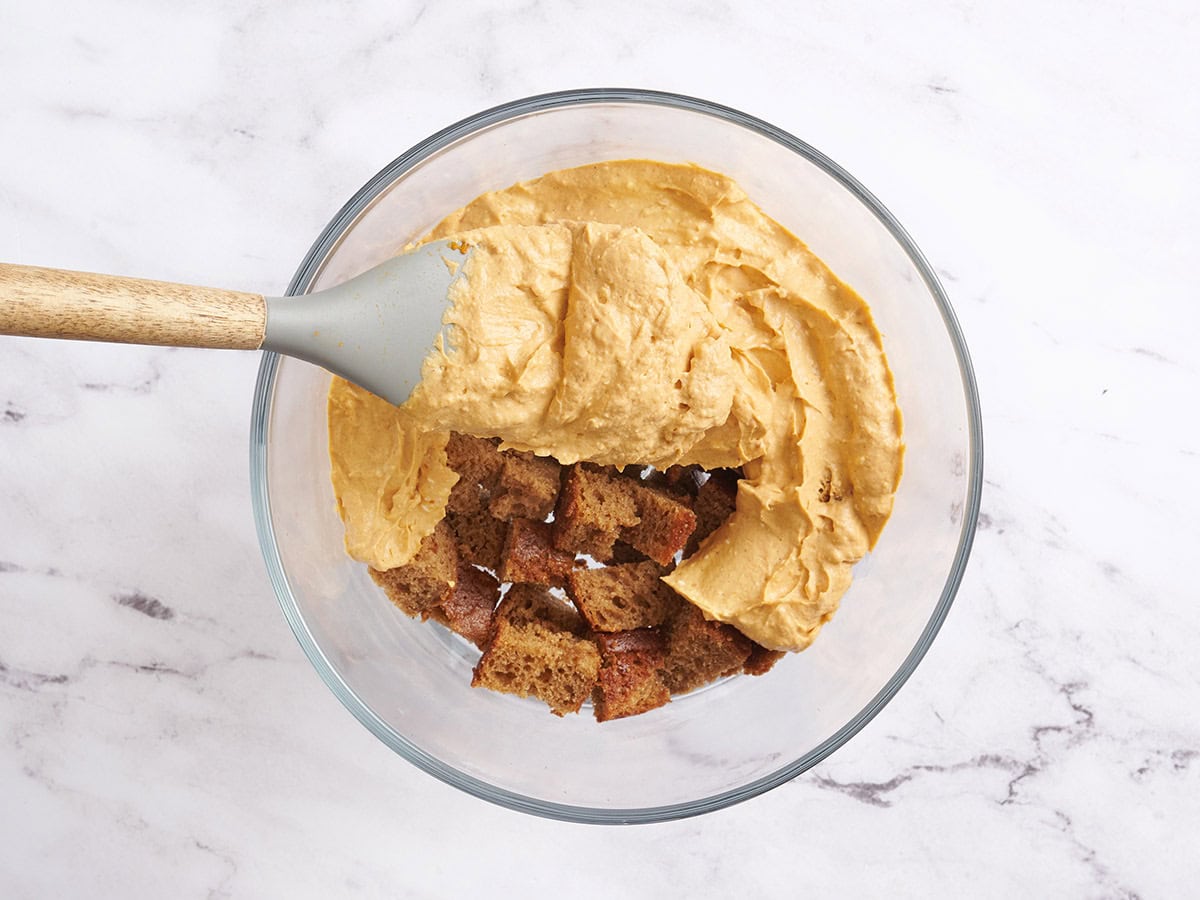 A pumpkin cream layer being spread over chopped spiced cake in a trifle bowl.