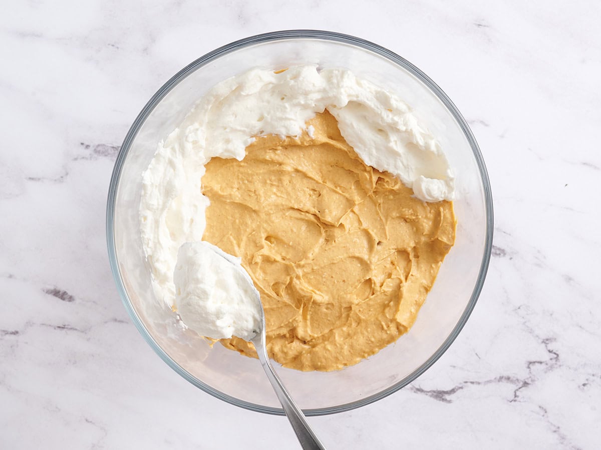 Whipped cream being spread over a pumpkin cream layer in a trifle bowl.