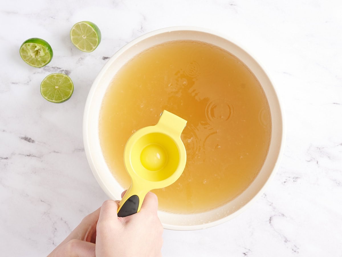 A lime being juiced into a bowl of ginger ale.