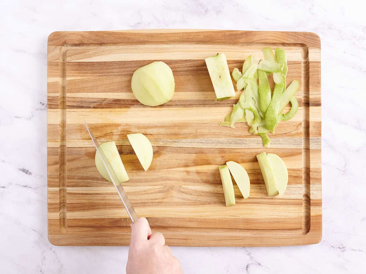 A green apple being sliced on a wooden cutting board.