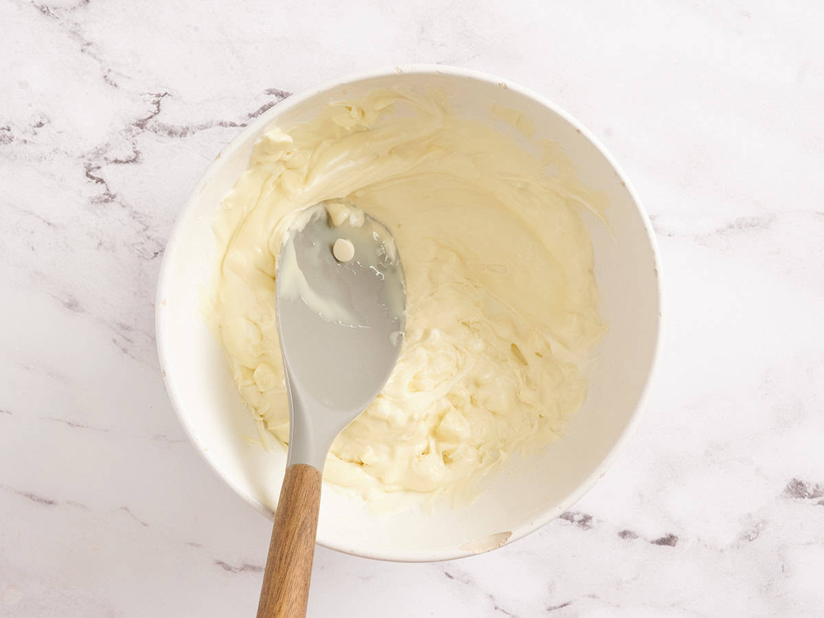 Melted white chocolate chips in a bowl being stirred with a spoon.