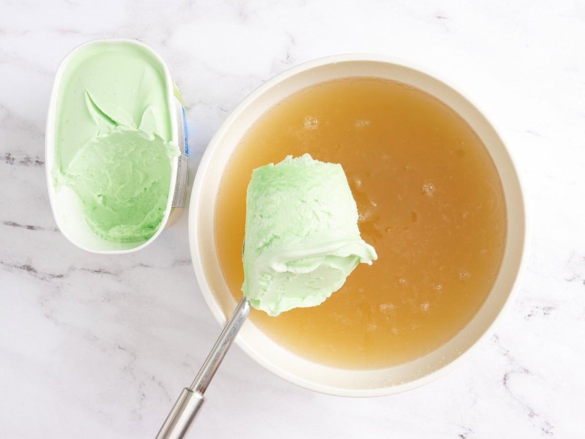 Lime sherbert being spooned into a bowl of halloween punch.