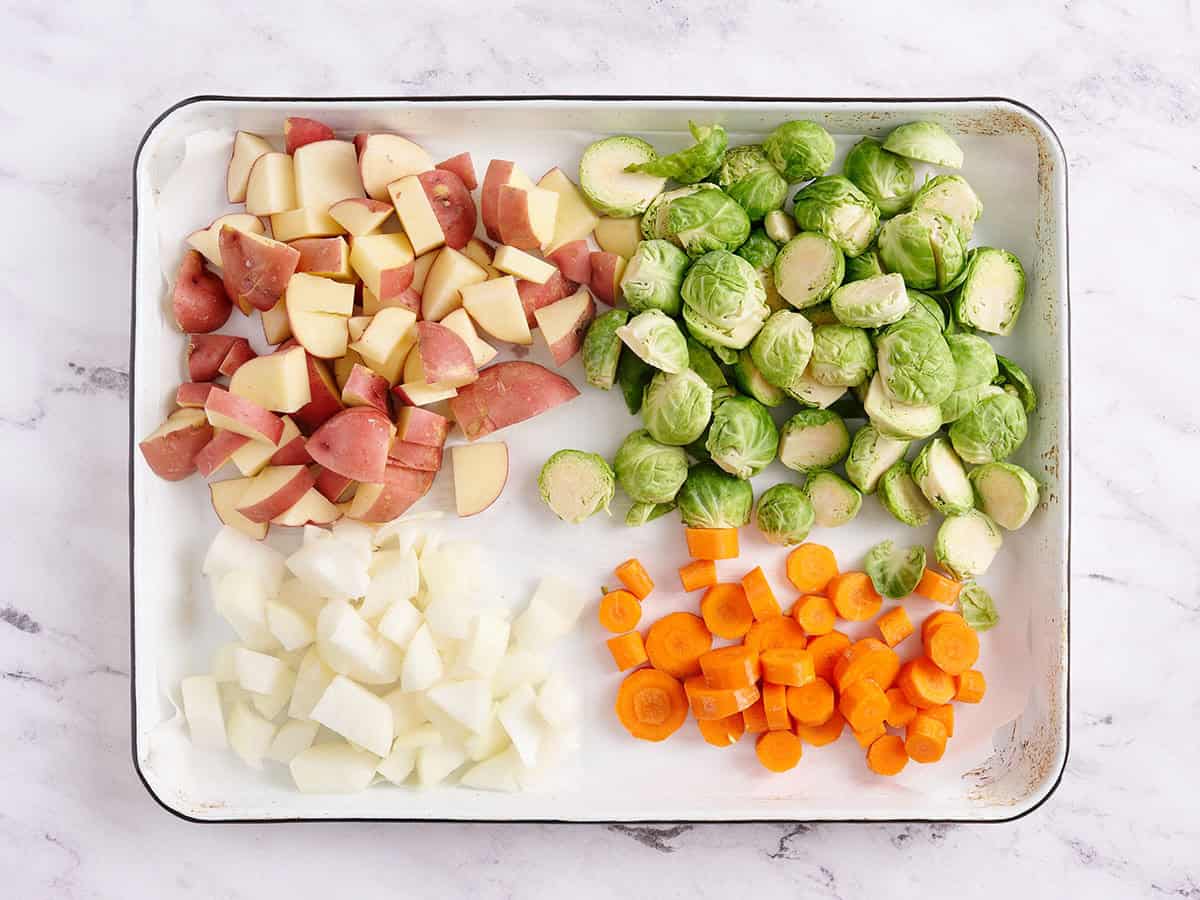 Brussels sprouts, red potatoes, apple, and carrots on a baking sheet.