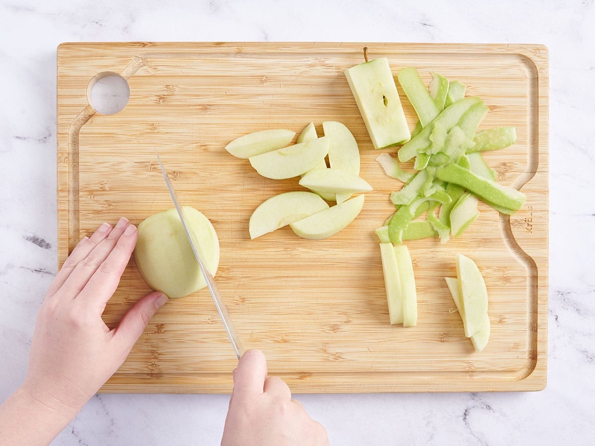 Apples being peeled and sliced on a cutting board.