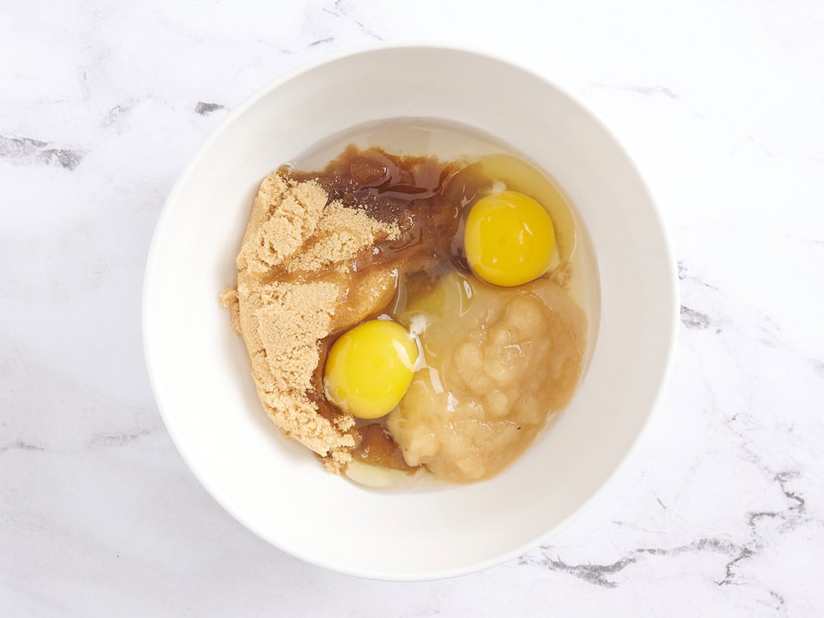 Brown sugar, eggs, and apple sauce in a mixing bowl.