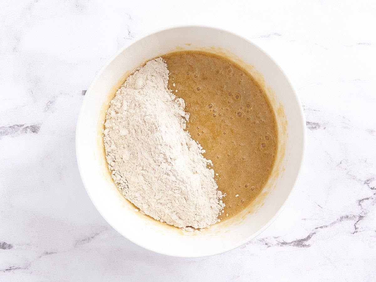 Dry ingredients added to a bowl of wet ingredients for spiced cake batter.