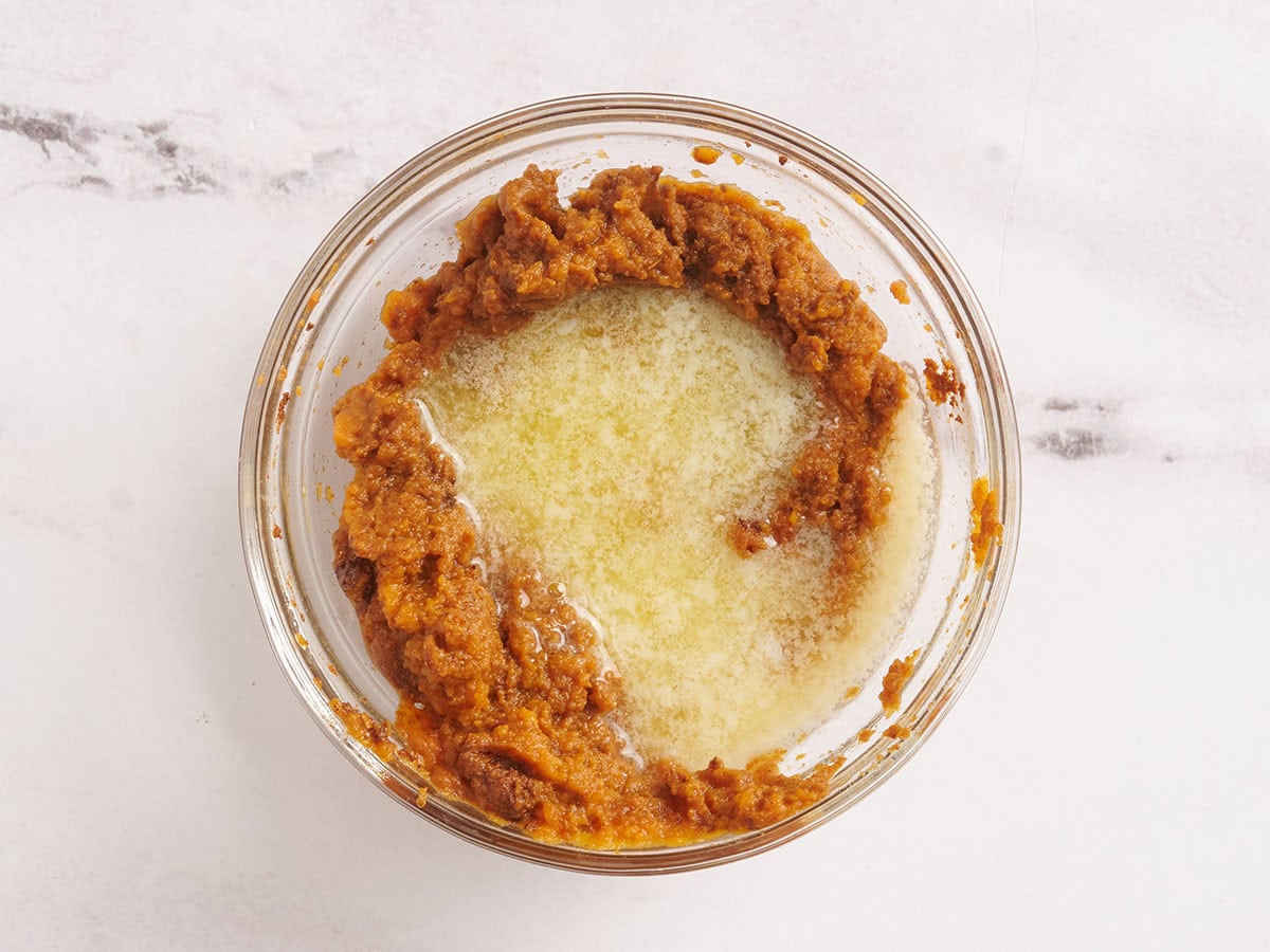 Melted butter added to a bowl of pumpkin puree and pumpkin spice.
