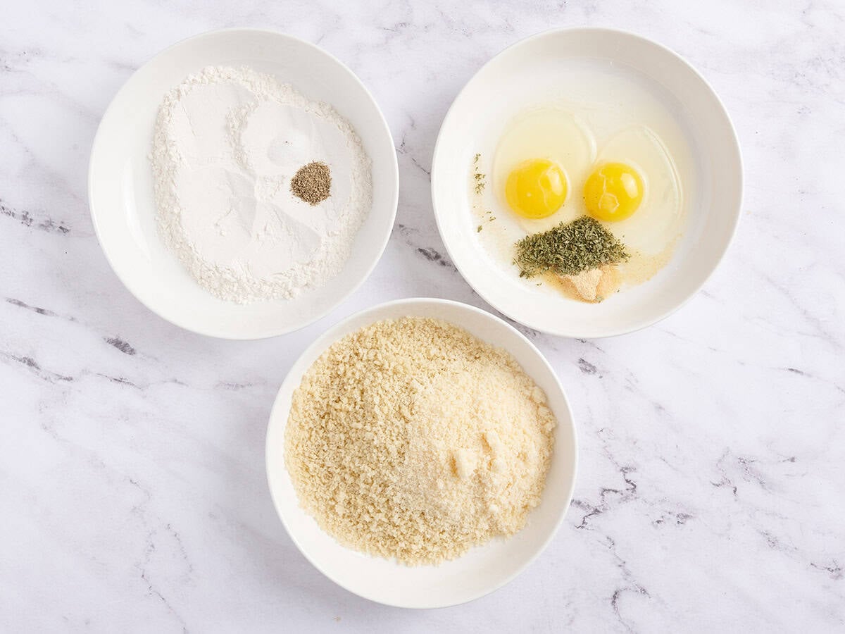 Three bowls, one with flour and seasonings, another with eggs and seasonings, and the last with panko breadcrumbs.