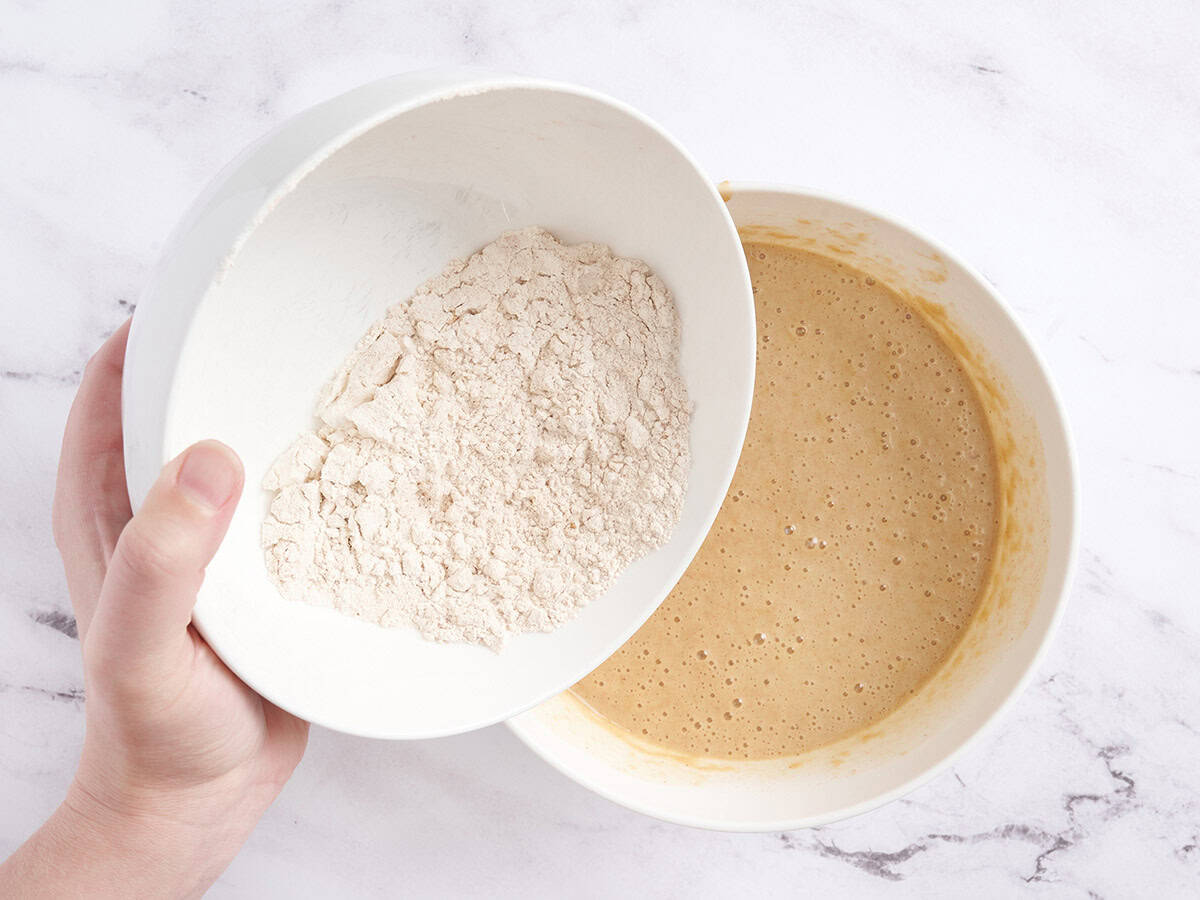 The dry ingredients for a spiced cake being poured into a bowl of wet ingredients.