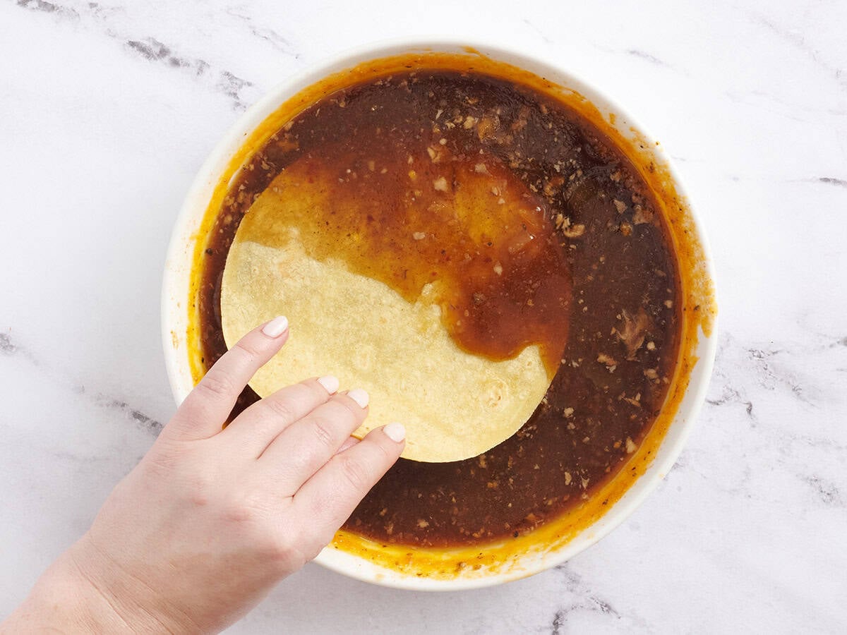 A hand dipping a corn tortilla in beef consome.