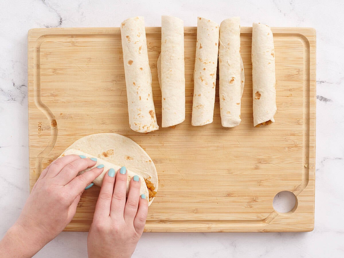Hands rolling up a flour tortilla to make a homemade apple flauta.