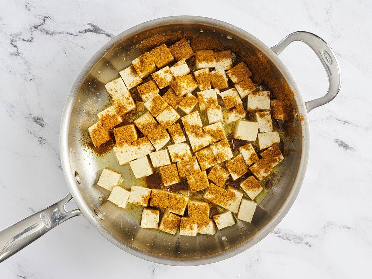 Spices added to a skillet with firm tofu cubes.