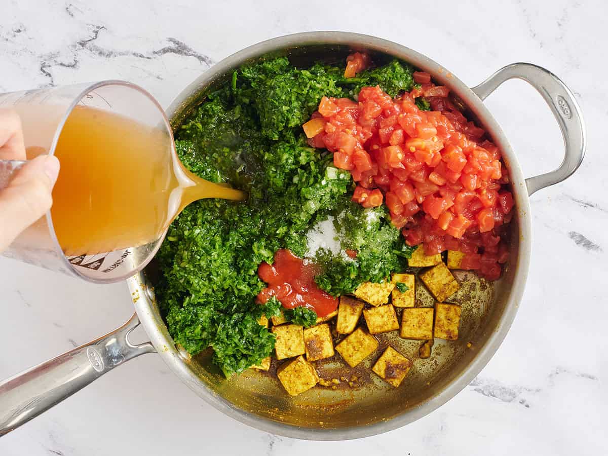Diced tomatoes, broth, and spinach pasta added to a skillet with tofu.