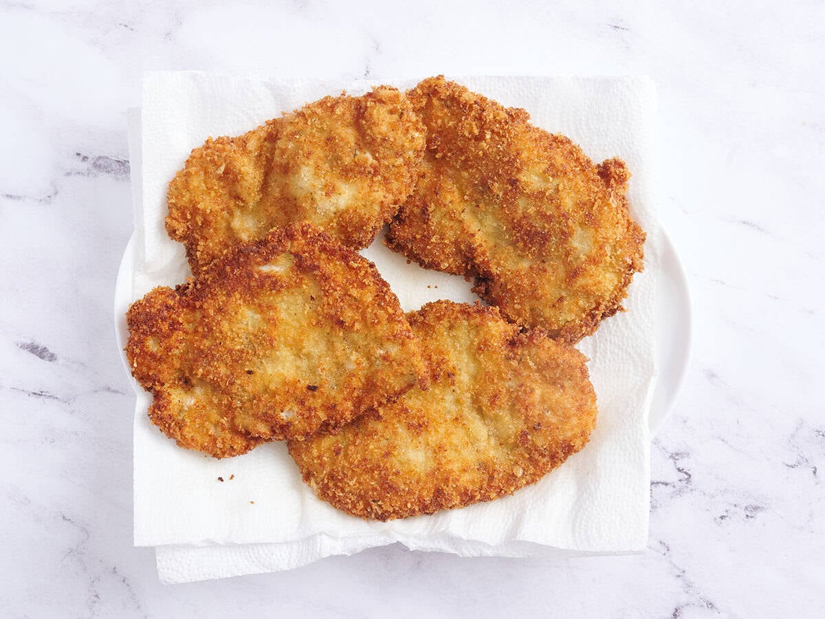 Four chicken schnitzels resting on paper towels.