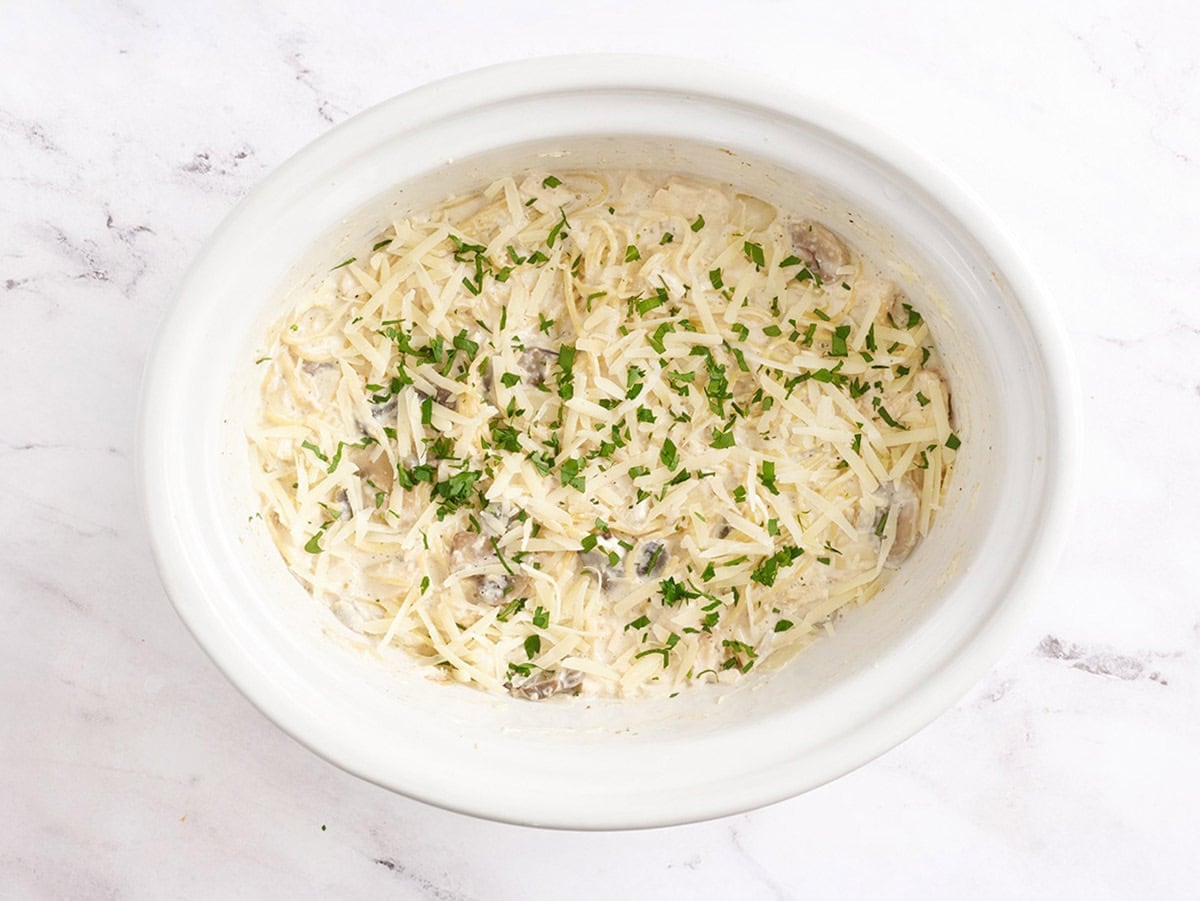 Crockpot chicken tetrazzini recipe in a slow cooker, topped with Parmesan and fresh parsley.