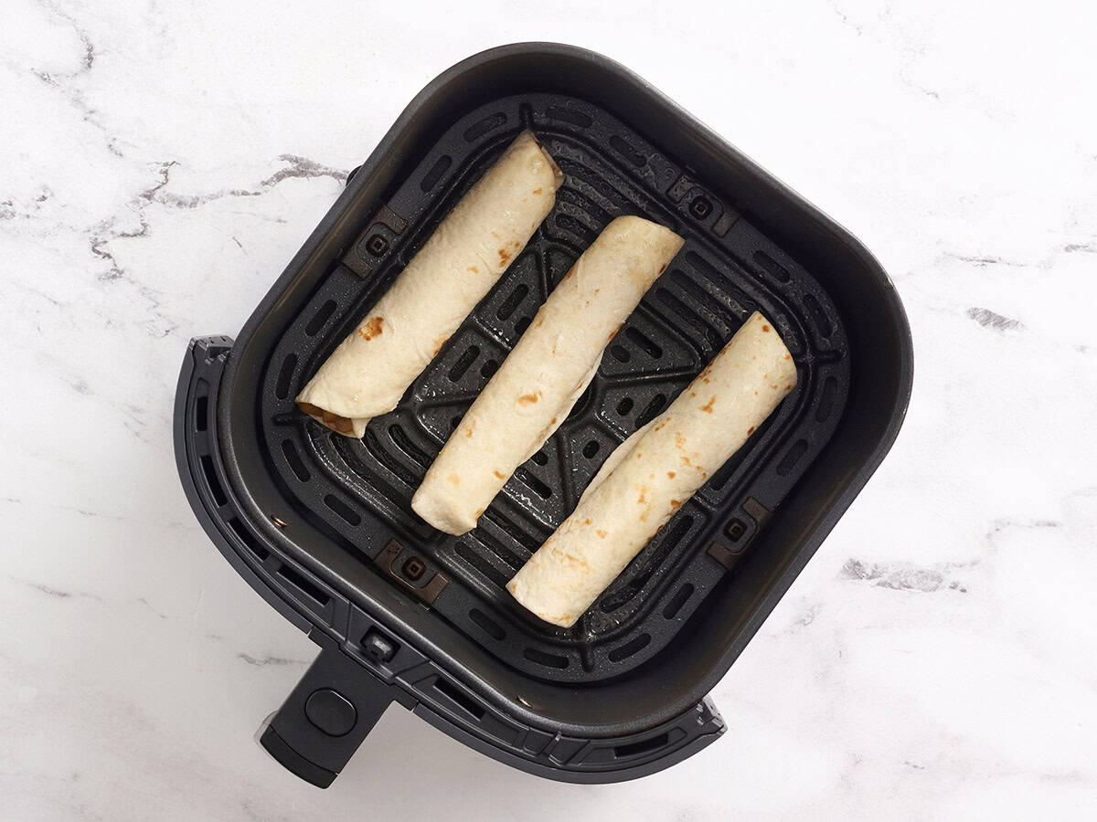 Apple flautas in an air fryer basket.