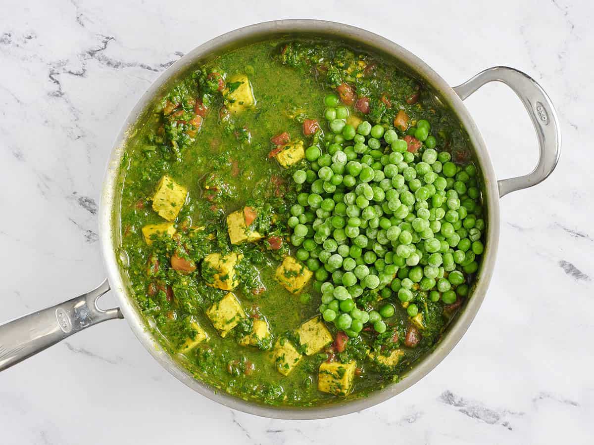 Frozen peas added to a skillet of tofu, spinach and green pea curry.