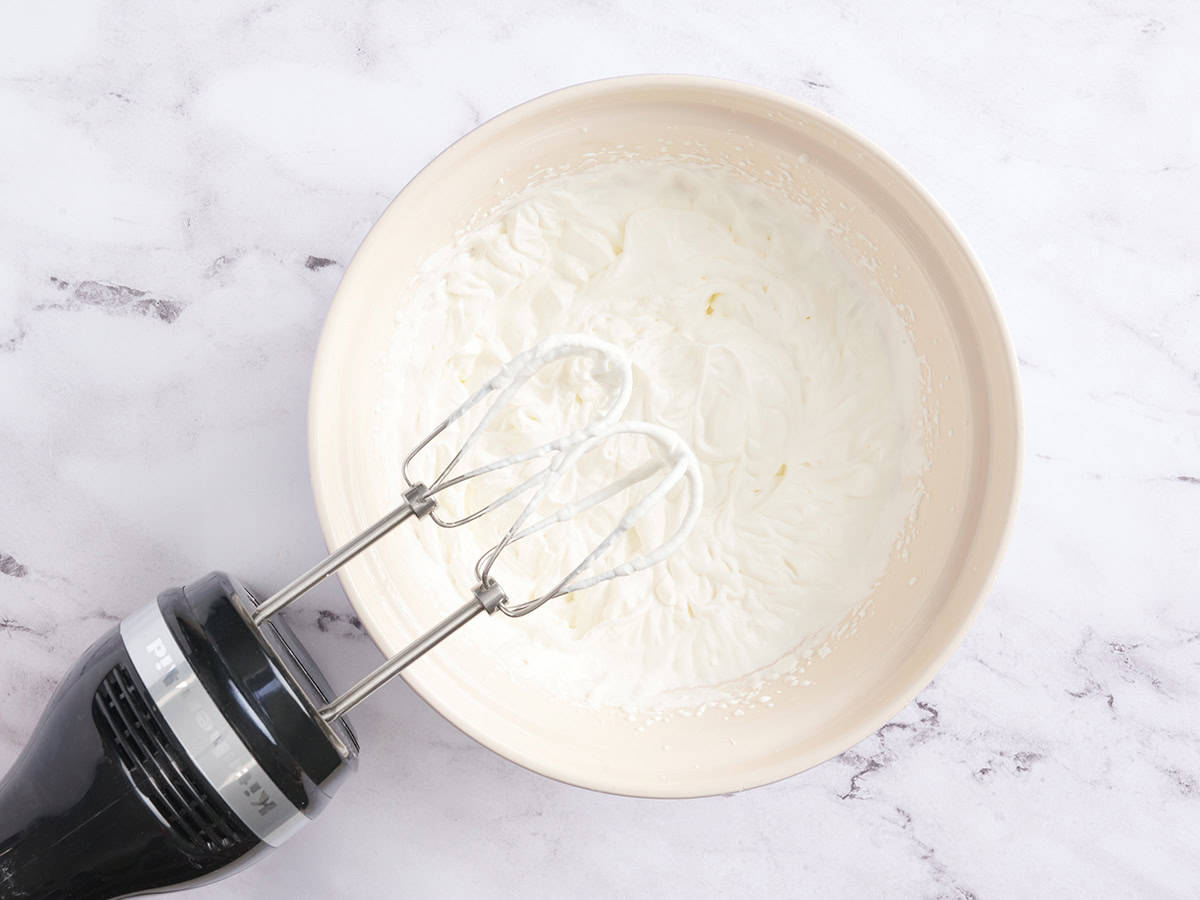A hand mixer with a bowl of whipped cream.