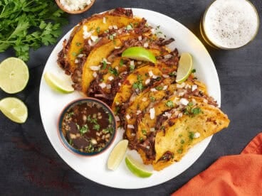 Overhead view of a plate of beef birria tacos with a bowl of consome.