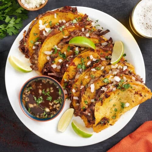 Overhead view of a plate of beef birria tacos with a bowl of consome.