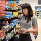 woman comparing two cans of tomato sauce at grocery store