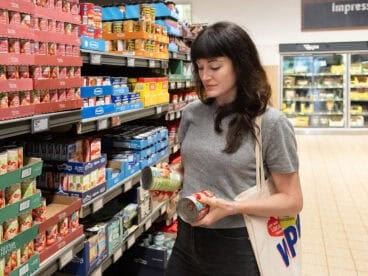 woman comparing two cans of tomato sauce at grocery store