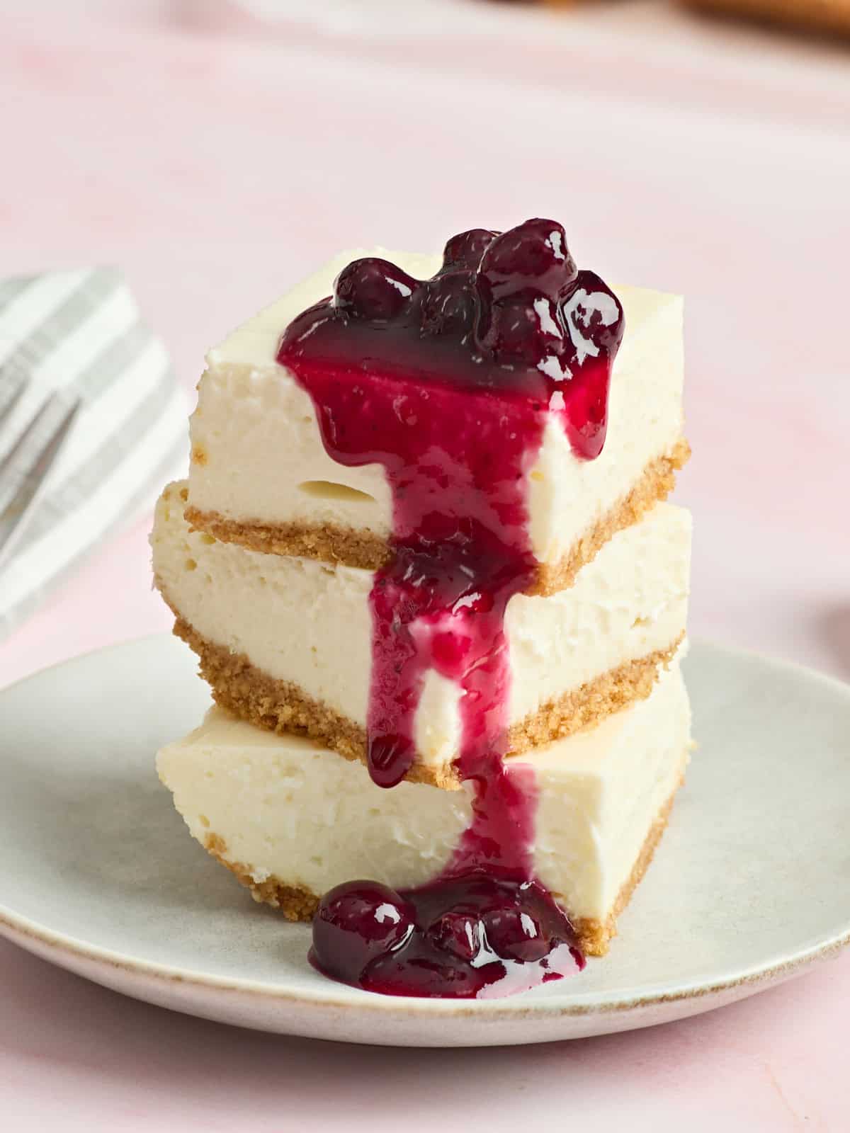 Cheesecake bars stacked on a plate and topped with blueberry sauce.