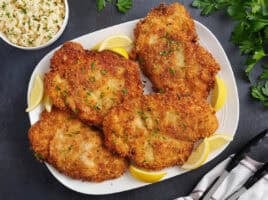 Overhead view of four chicken schnitzels on a plate.