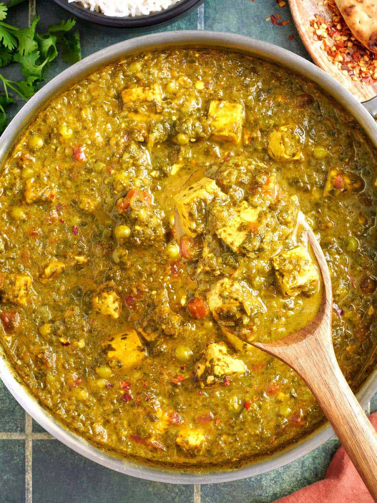 Overhead view of tofu, spinach, and pea curry in a skillet with a wooden spoon.