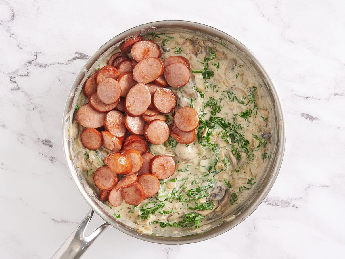 Browned sliced turkey sausage added to a creamy kale and mushroom sauce in a skillet.