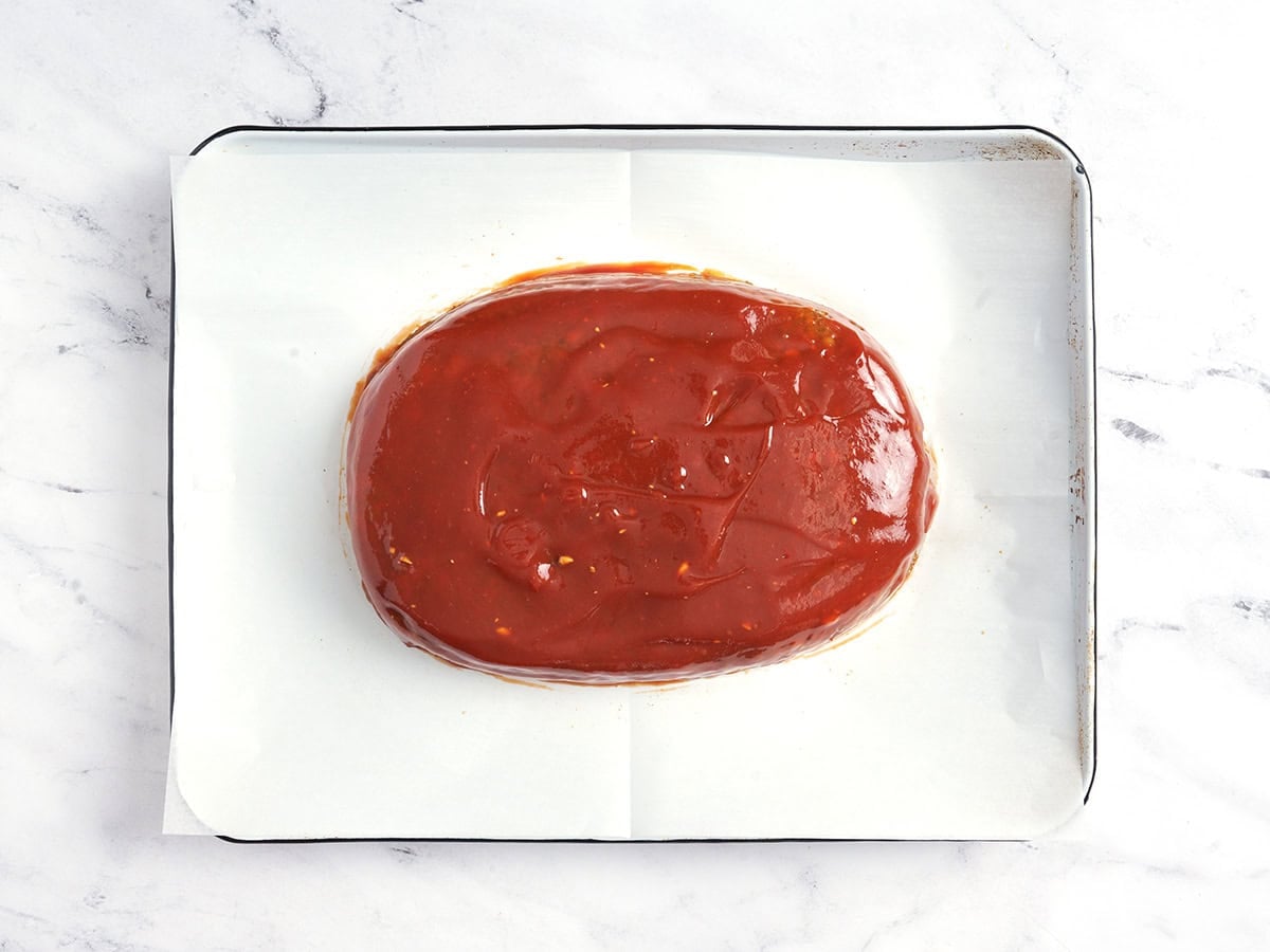 A lentil meatloaf on a parchment lined baking sheet topped with glaze.