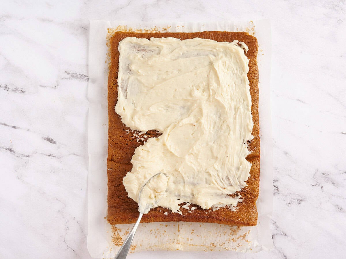 cream cheese frosting being spread on pumpkin roll