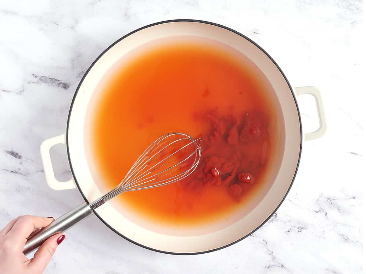 Water and tomato being whisked together in a bowl.