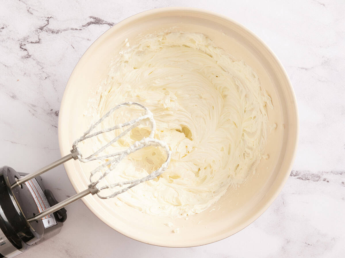 Beaten cream cheese in a bowl with a hand mixer.