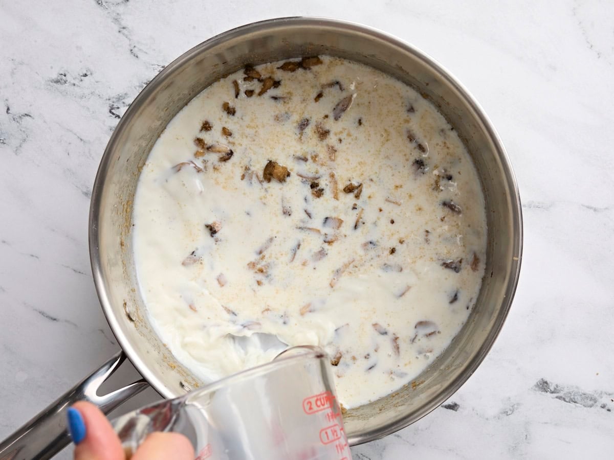 Cream being poured into a skillet to make cream of mushroom soup.