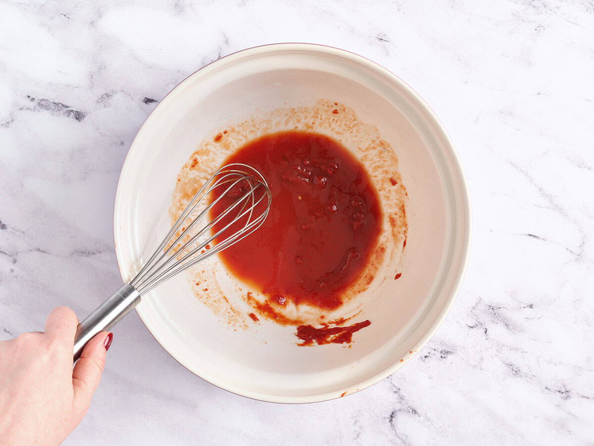 Pasta water and tomato paste being whisked together in a bowl.