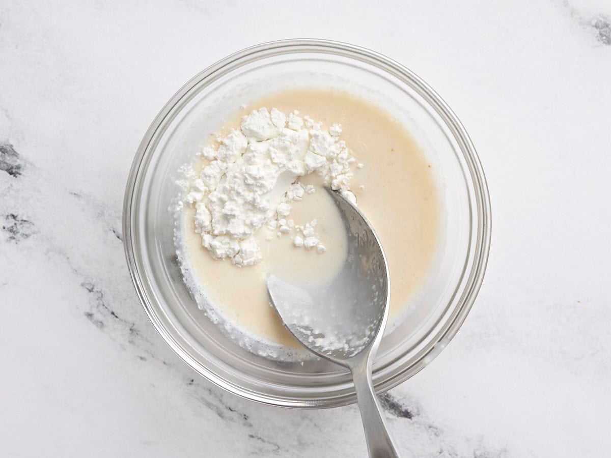A spoon mixing cornstarch to make a slurry.