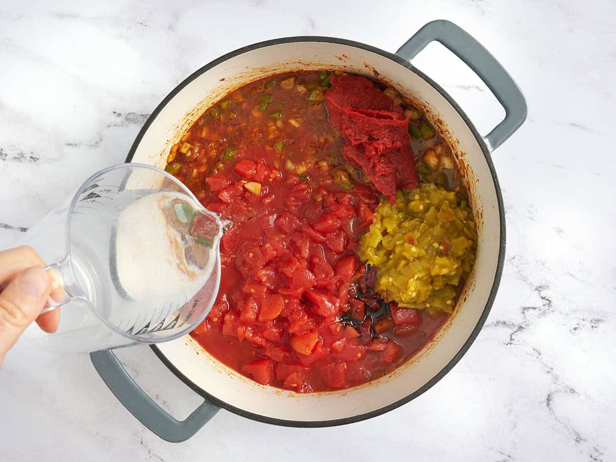ingredients for vegetarian chili being added to a pot as someone pours in water