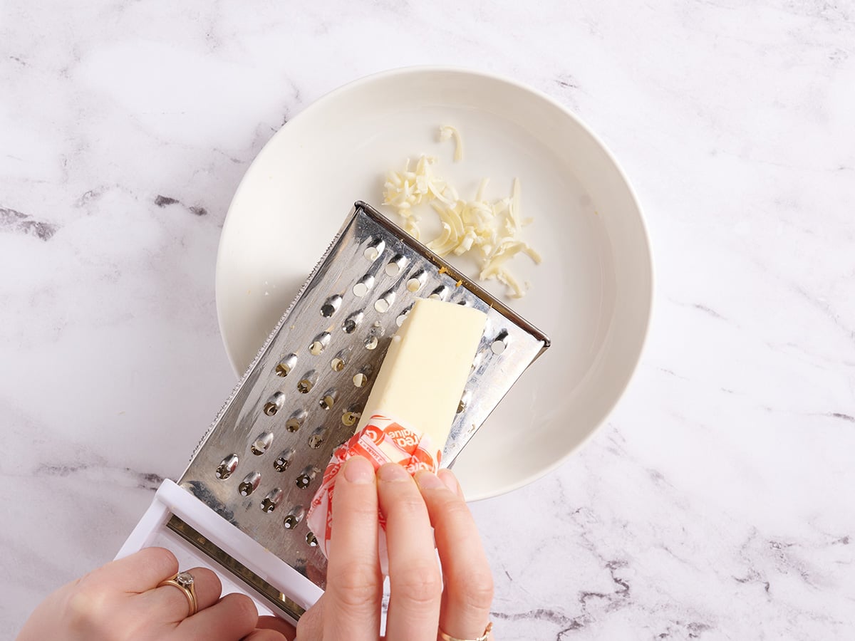 A hand using a grater to shred butter.