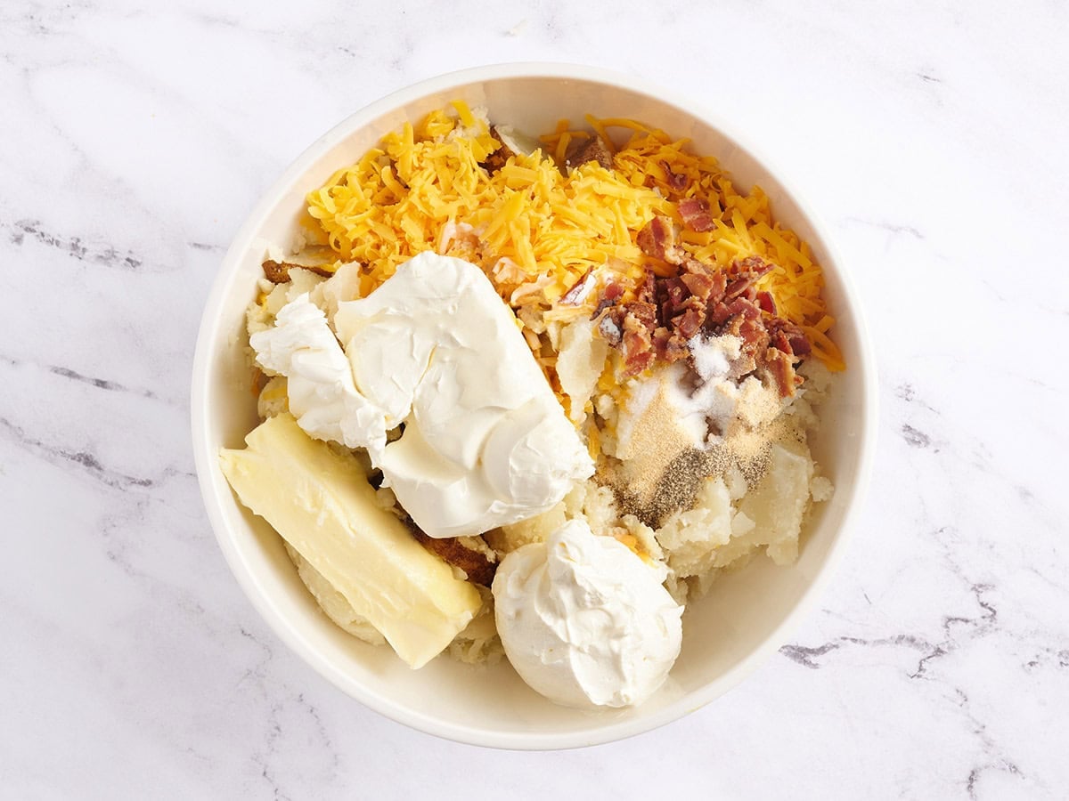 Potato, cheese, bacon, sour cream, cream cheese and butter in a bowl.