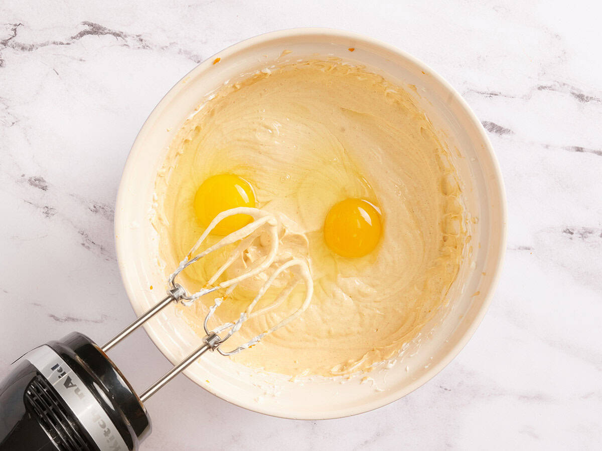 Eggs added to pumpkin cheesecake filling in a bowl.