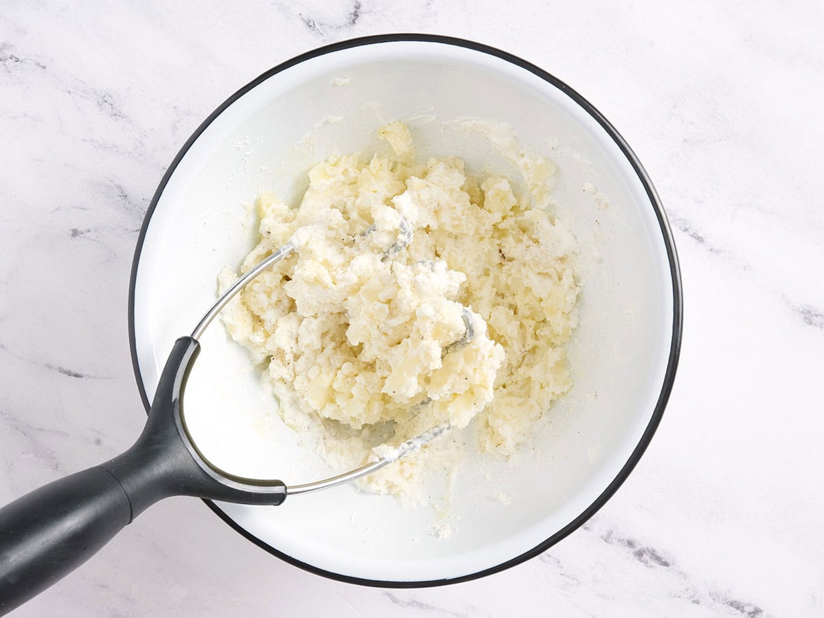 Potato skin filling in a bowl with a potato masher.