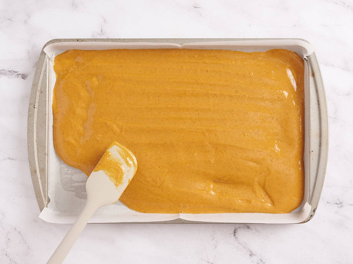batter for pumpkin roll being spread on a baking tray