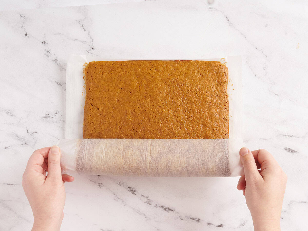 pumpkin roll cake being rolled with parchment paper