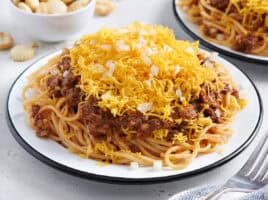 Side view of a plate of Cincinnati chili with shredded cheese and diced onions.